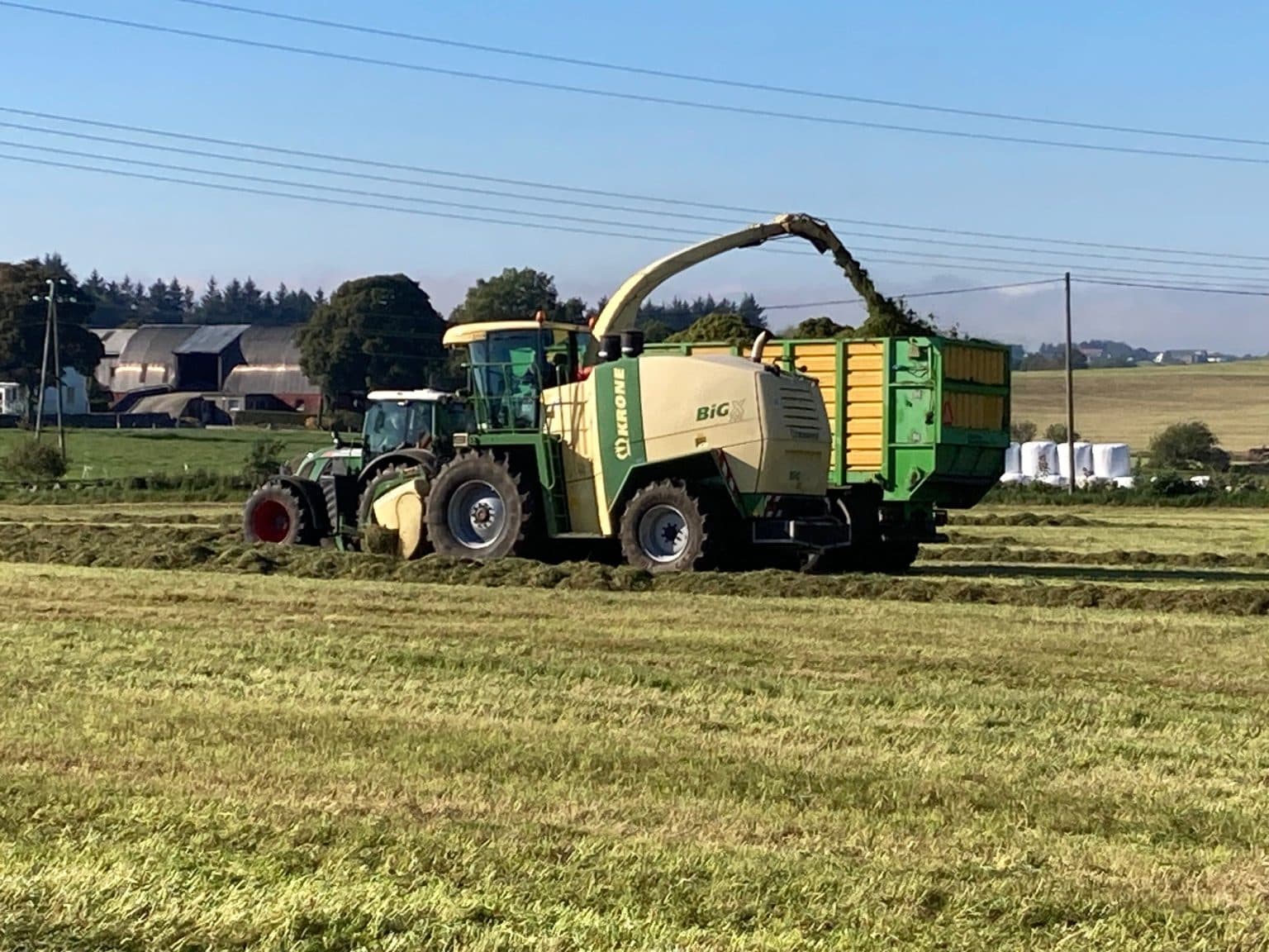 Finsnitter og traktor i arbeid med grasavling på jordet